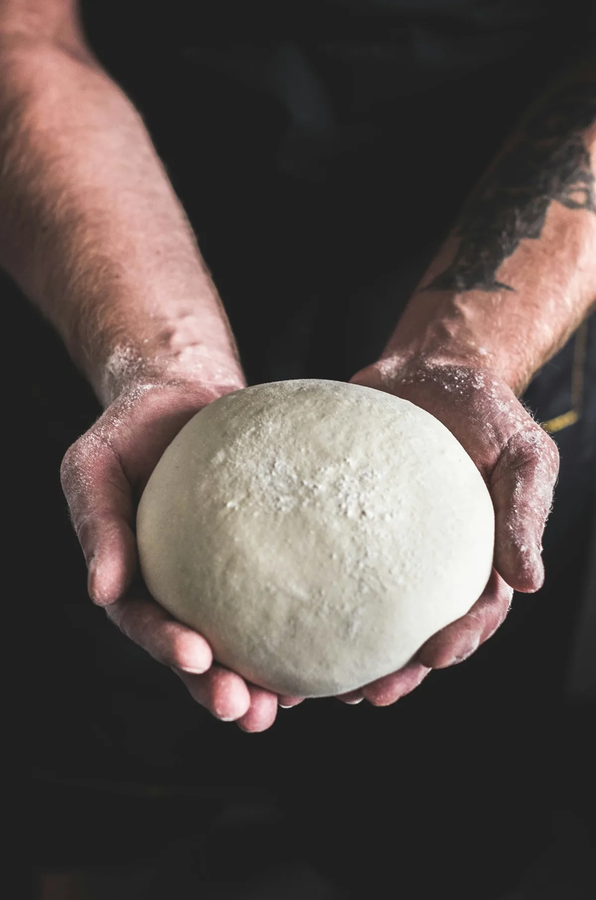 A ball of pizza dough held in floured hands before shaping