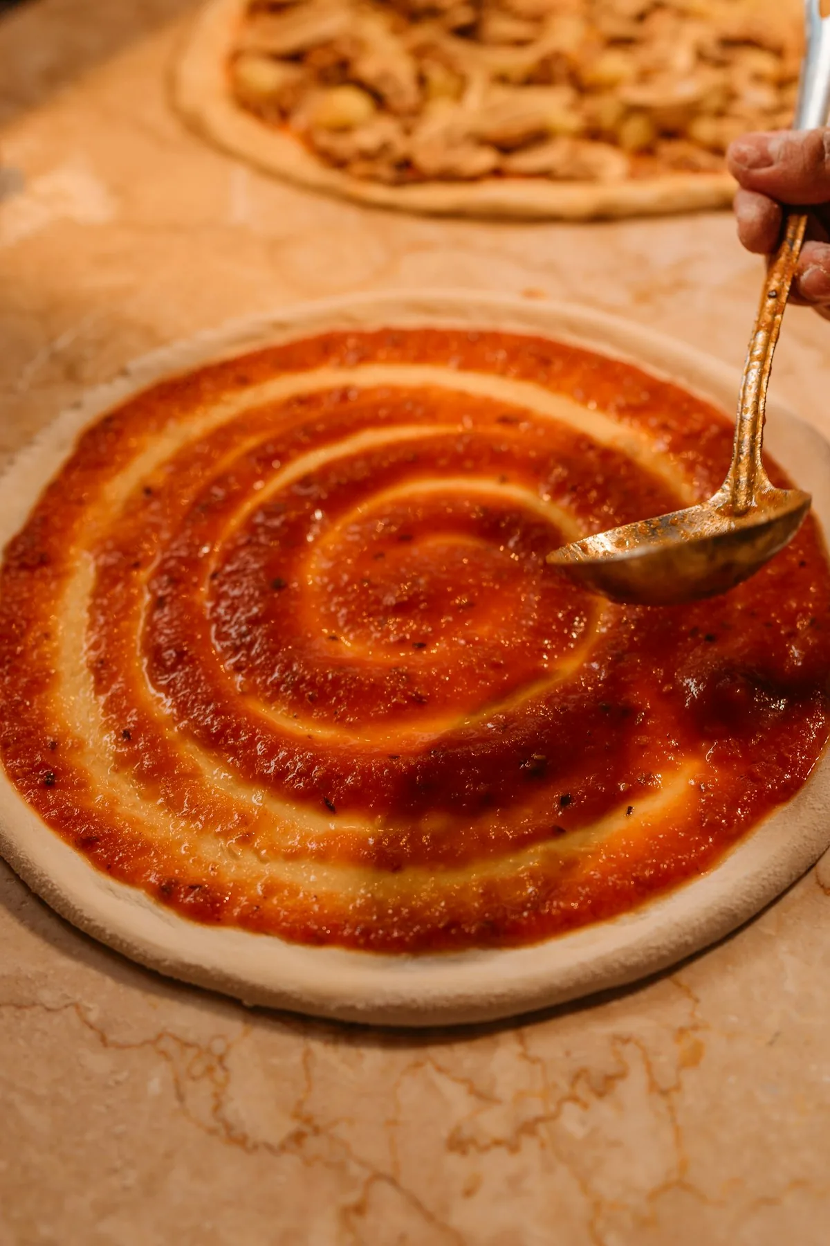 Tomato sauce being spread in a spiral over round pizza dough